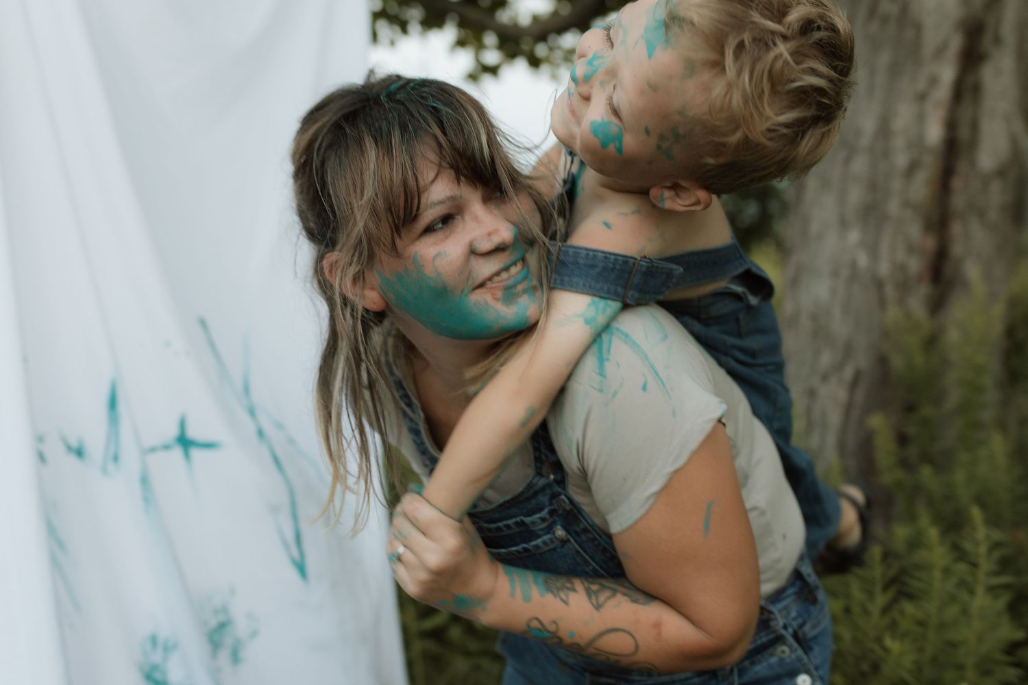 A mom holds her laughing son on her back as they are both covered in paint from a paint session by Courtice family photographer