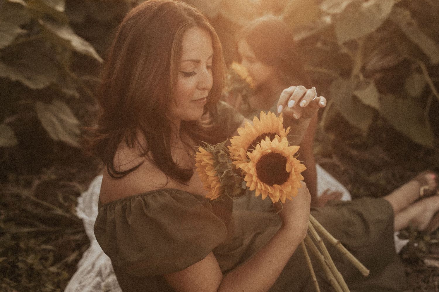 An artistic photo of a woman looking closely at a sunflower while her daughter is in the background by Durham Region family photographer