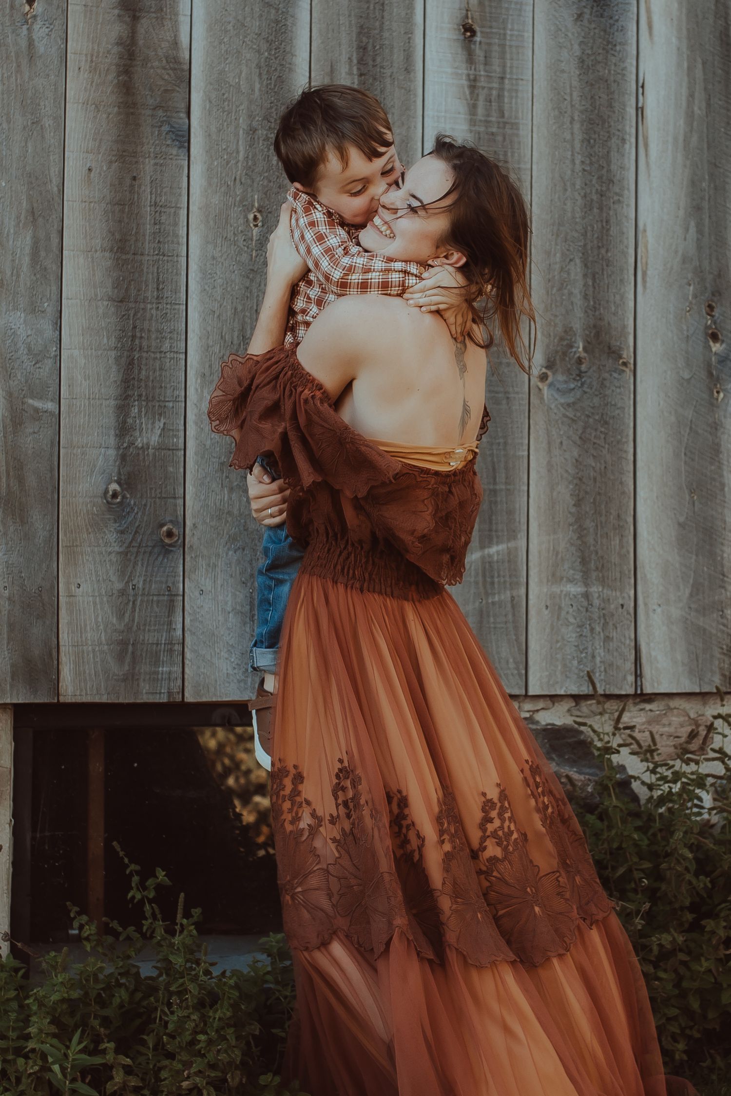 A romantic couple embraces in front of a rustic wooden fence while wearing brown and blue coordinated outfits.