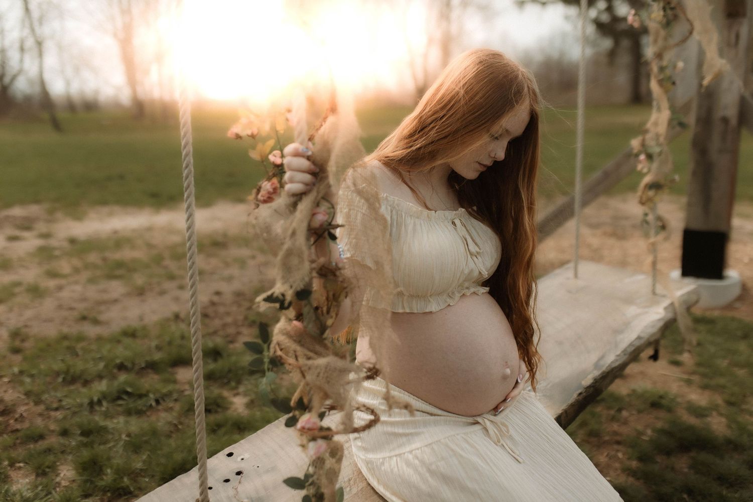 Ethereal image of a pregnant woman sitting on a swing in the sunshine looking at her baby bump by Bowmanville, ON family photographer.