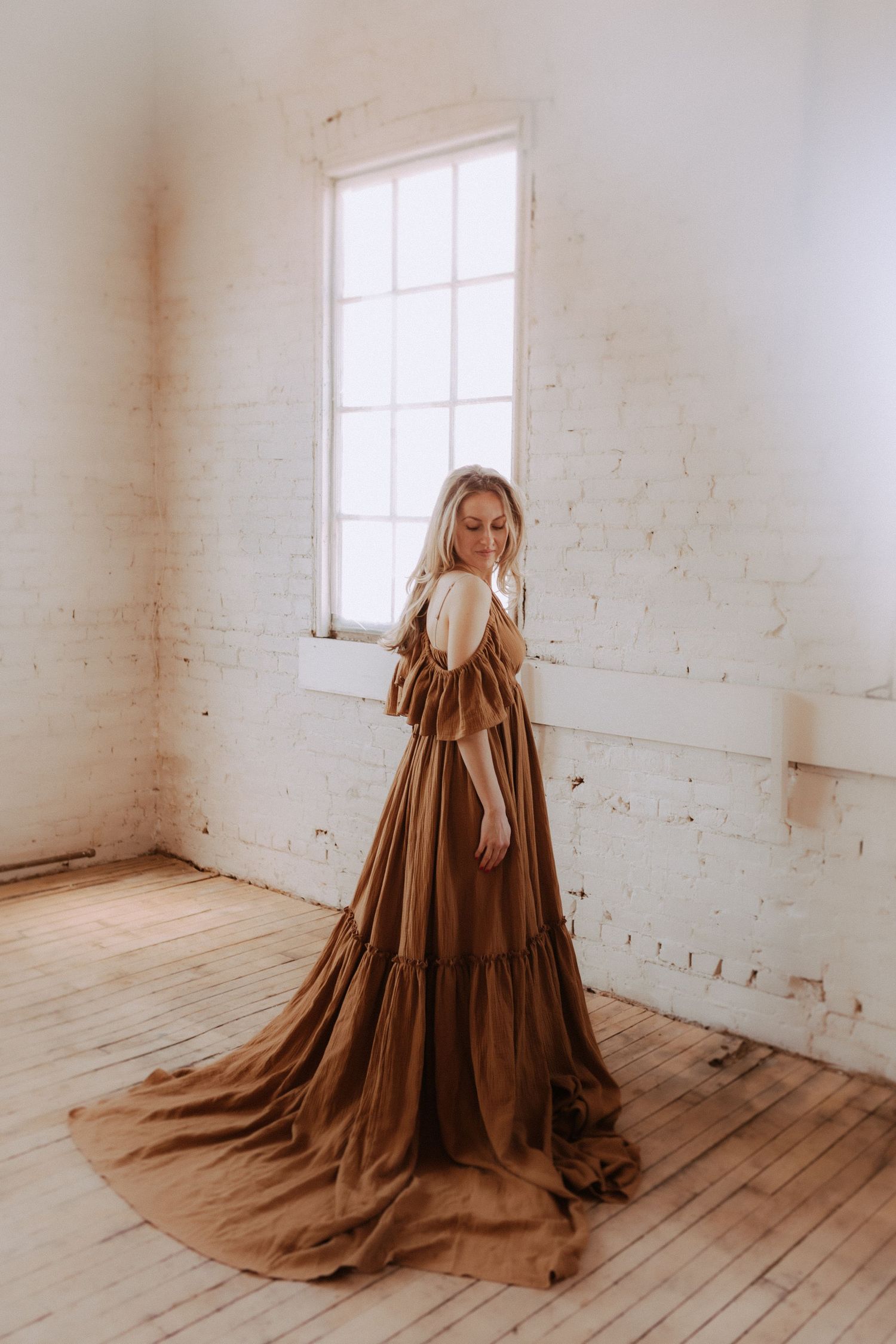 Dramatic brown gown with full skirt photographed in bright minimalist room with wooden floors.