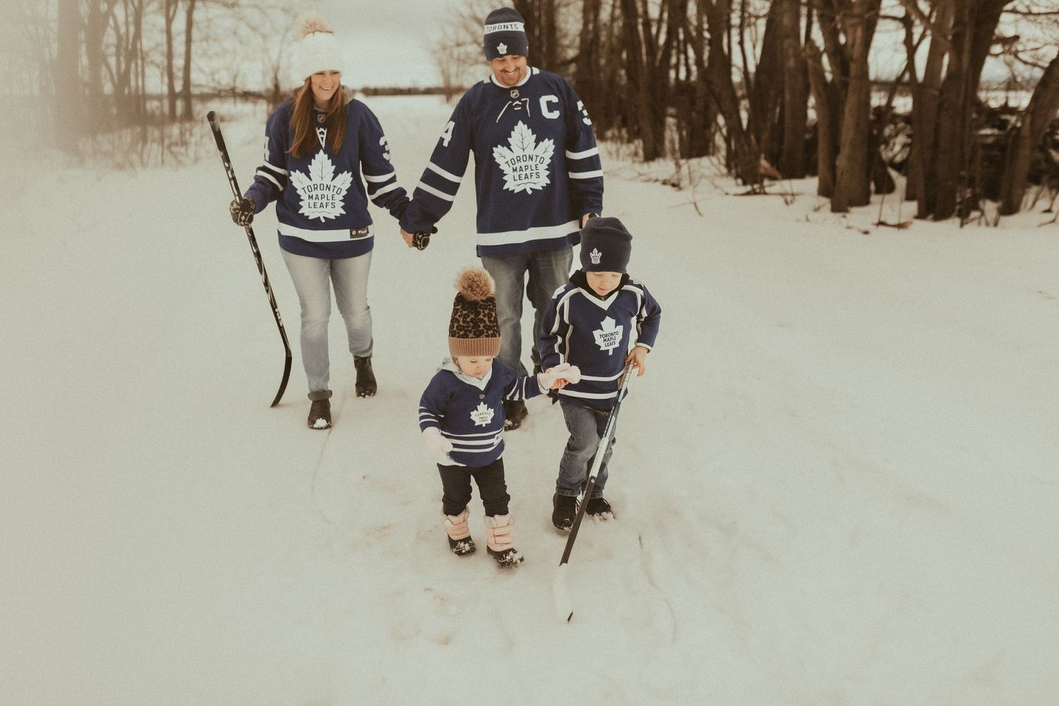 winter session of a family in hockey jerseys playing together in the snow by Bowmanville Family Photographer