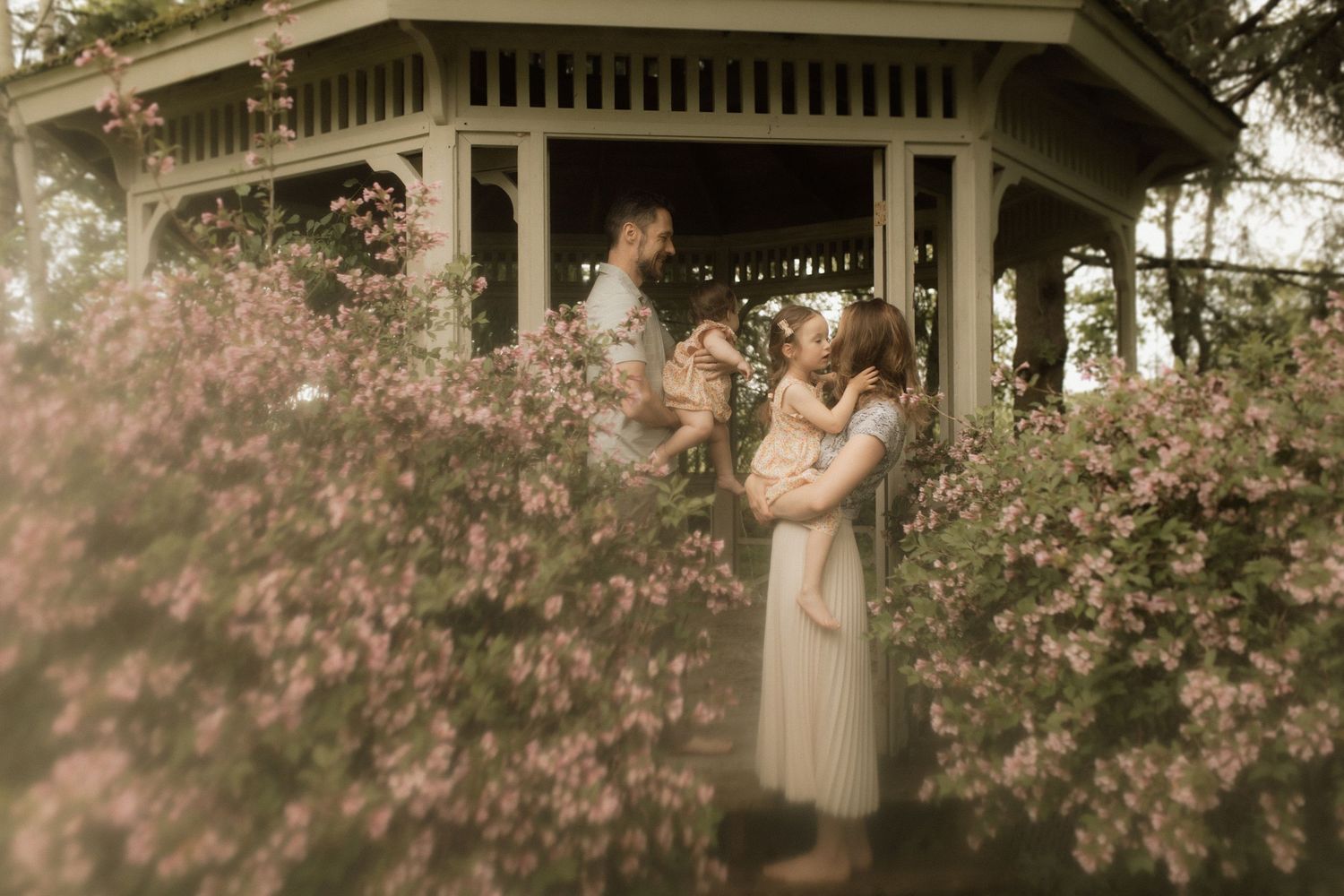 Nostalgic image of a family in a gazebo surrounded by springtime blossoms by  Bowmanville, ON family photographer.