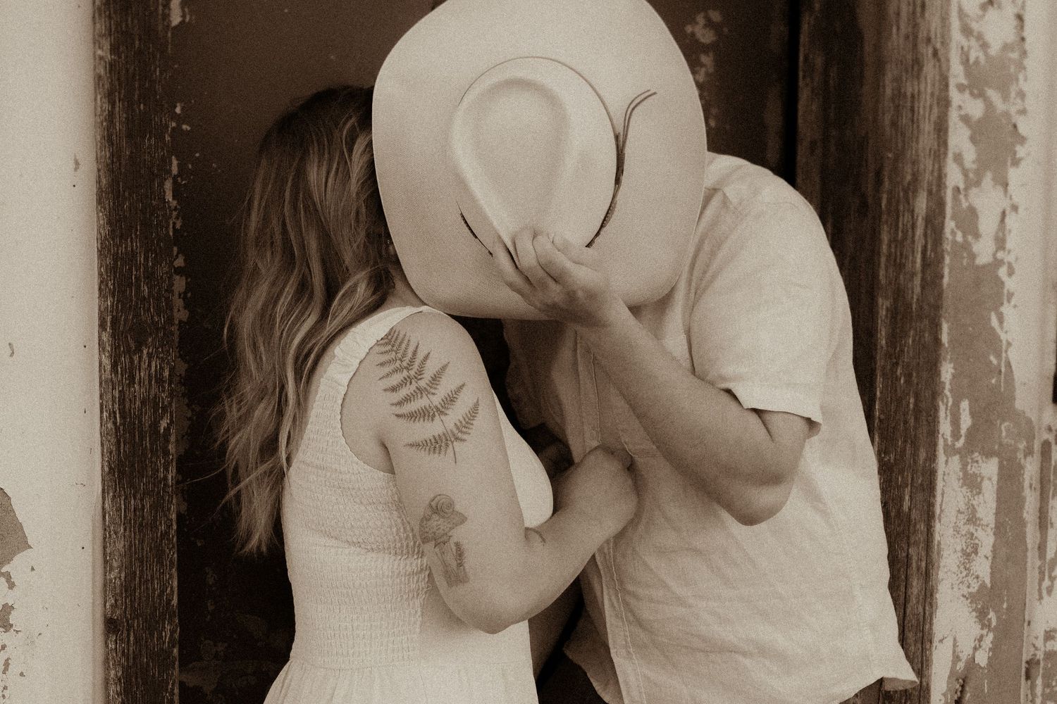 Couple kissing behind cowboy hat in Orono Ontario countryside by Orono family photographer”