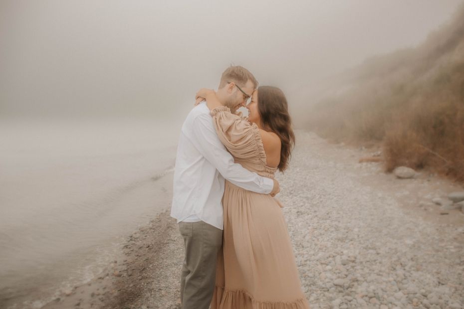 Couple embracing on a foggy beach in a romantic, dreamy photoshoot taken by your Cobourg, ON family photographer