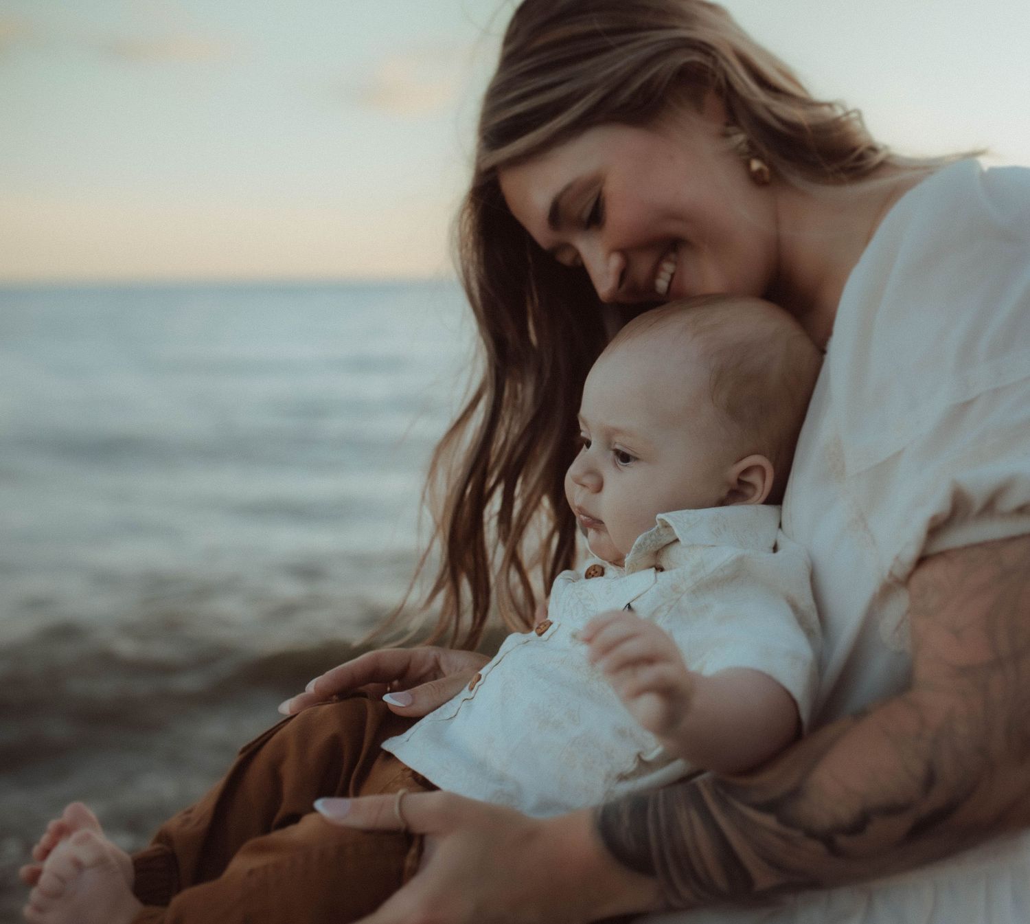 Young mom holding her baby boy in her arms with an expression of pure joy during a summer sunset by Bowmanville, ON family photographer