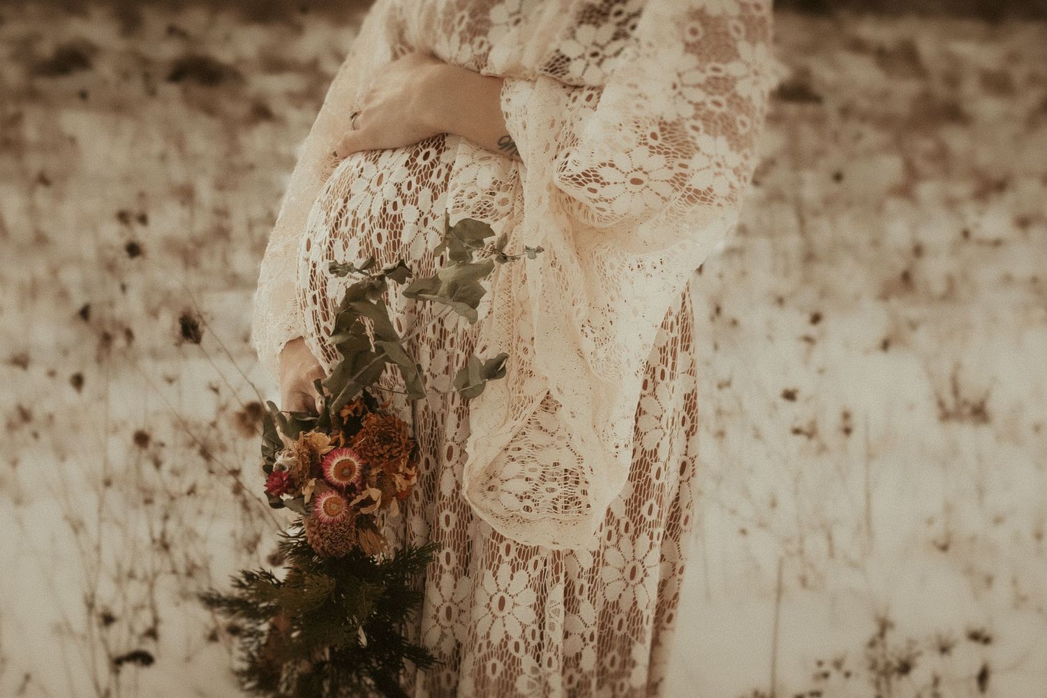 A pregnant woman in a white lace dress holding dried flowers and her baby bump taken by a Bowmanville, ON family photographer