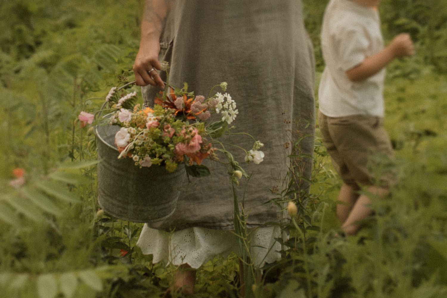 Mother carrying flowers beside her toddler in a field during a family photography session in Bowmanville, Ontario