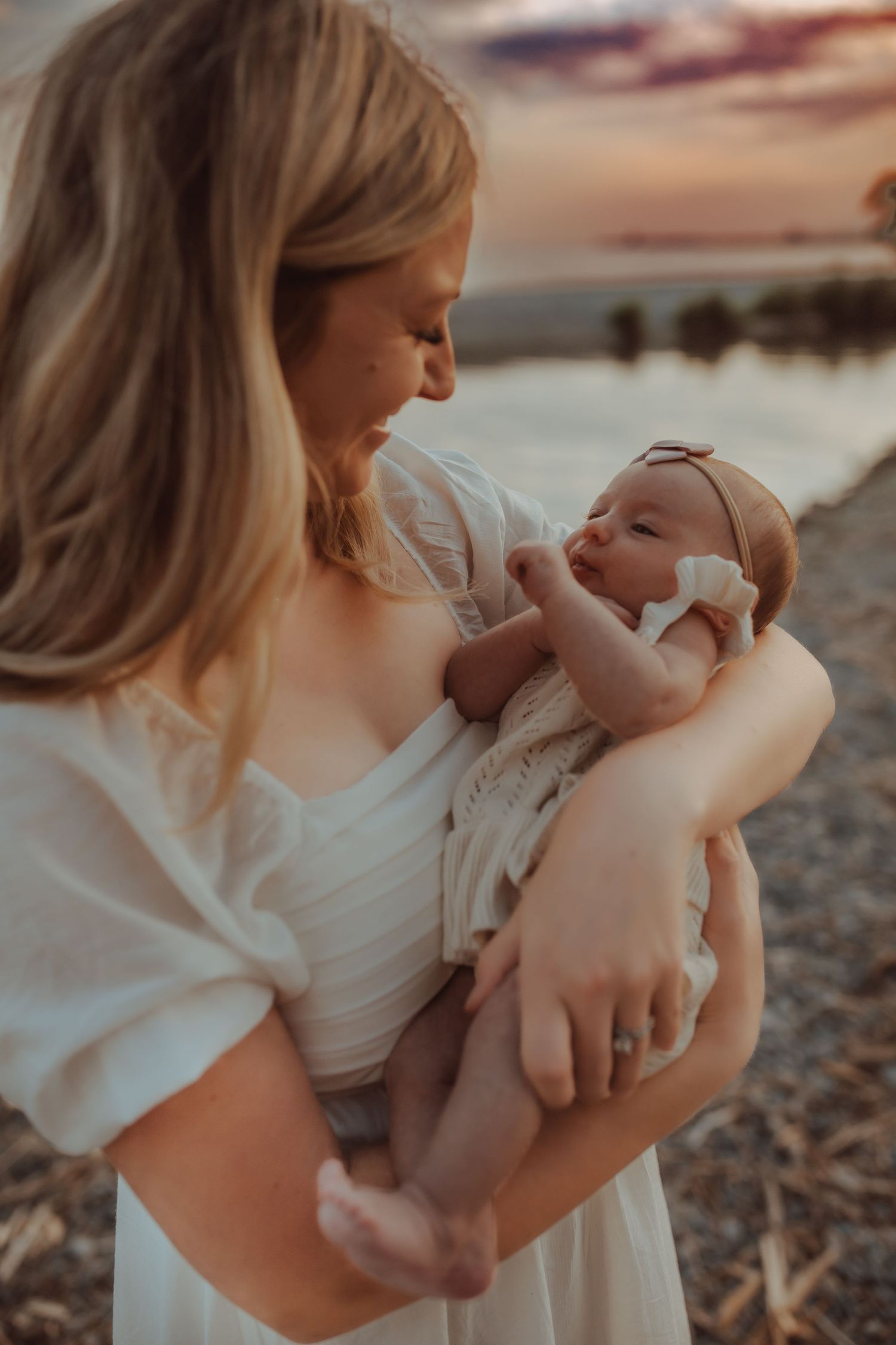 Young mom cradling her baby girl on a beach at sunset in the summer by Bowmanville, ON family photographer