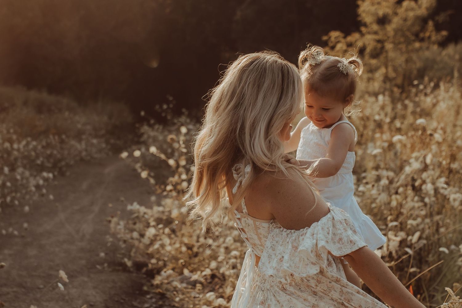 mother cradling her daughter in a field of wild flowers in early morning light by Bowmanville maternity photographer