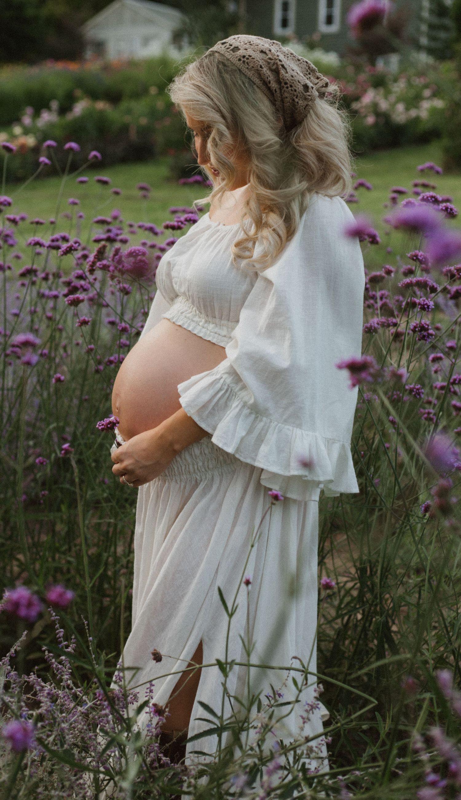 Ethereal maternity photo in a garden with white dress and purple flowers in soft light taken by Bowmanville, ON family photographer