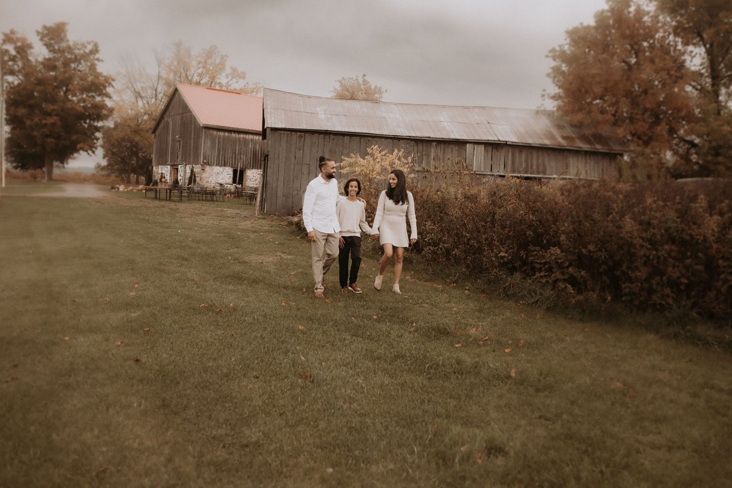 A mom and dad with a teenager walking together in a field beside a rustic barn by Courtice, ON family photographer