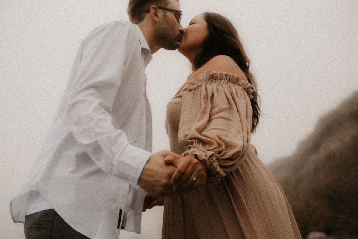 Engaged couple kissing on a foggy beach, with the woman wearing a flowy dress, by artistic family photographer Bowmanville, ON.