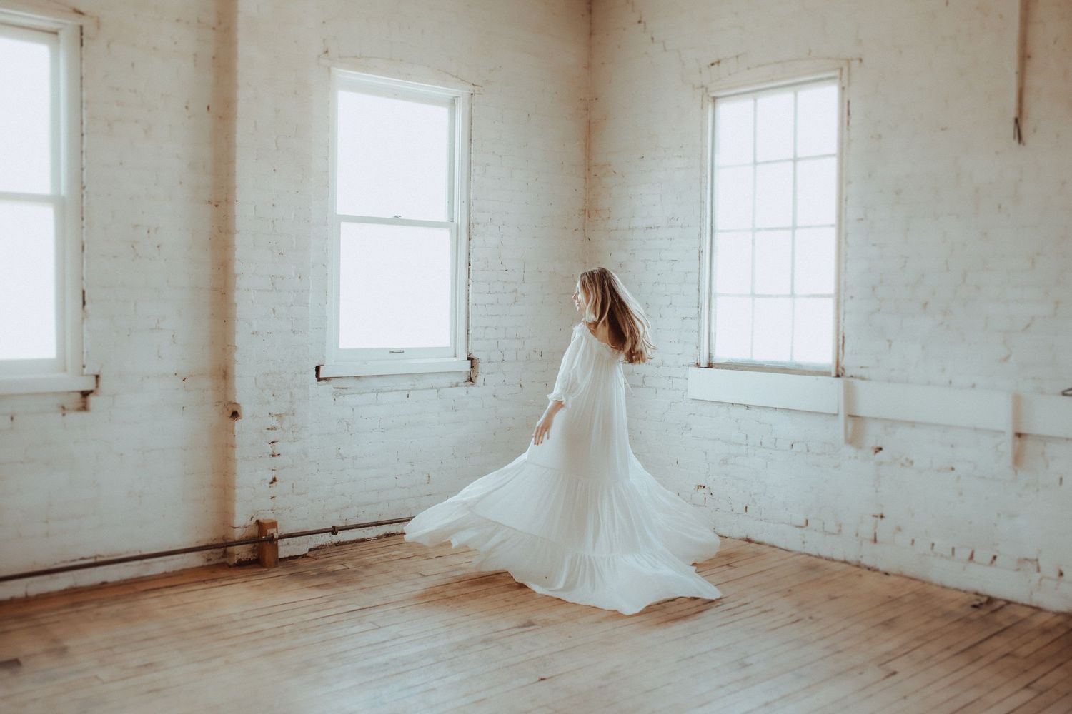 Airy white studio space with hardwood floors and multiple windows casting natural light.