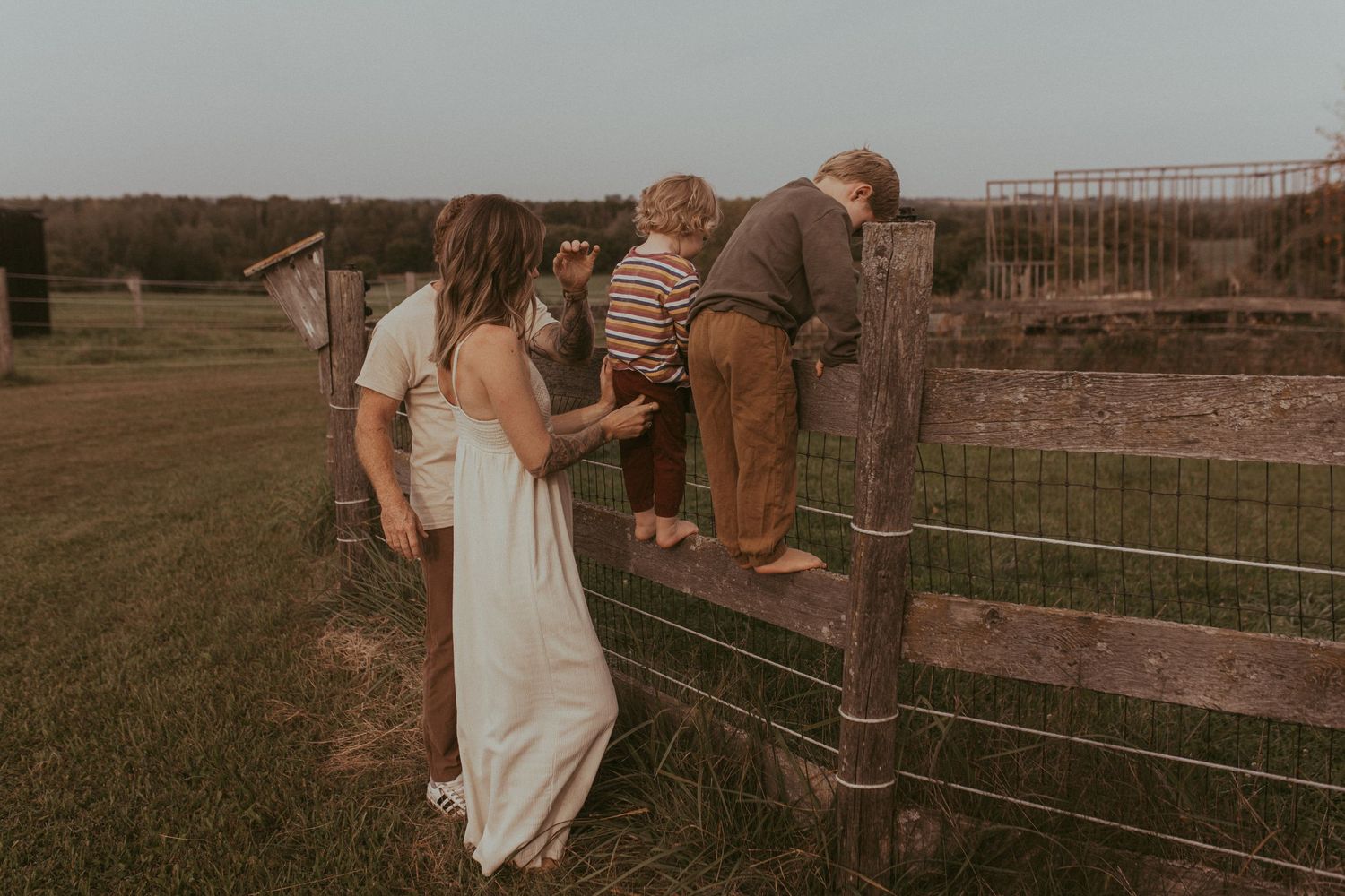 Parents watching their young boys climbing a fence in their yard by Durham Region maternity photographer