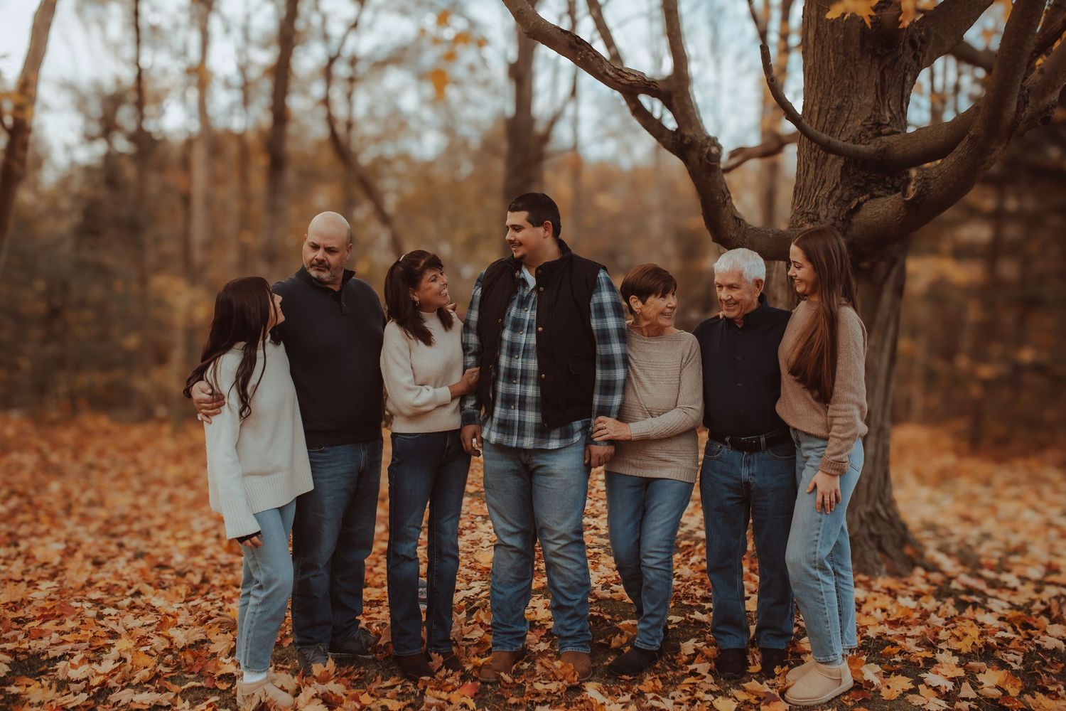 Fall photo of an extended family standing together surrounded by colourful leaves taken by Bowmanville Family Photographer