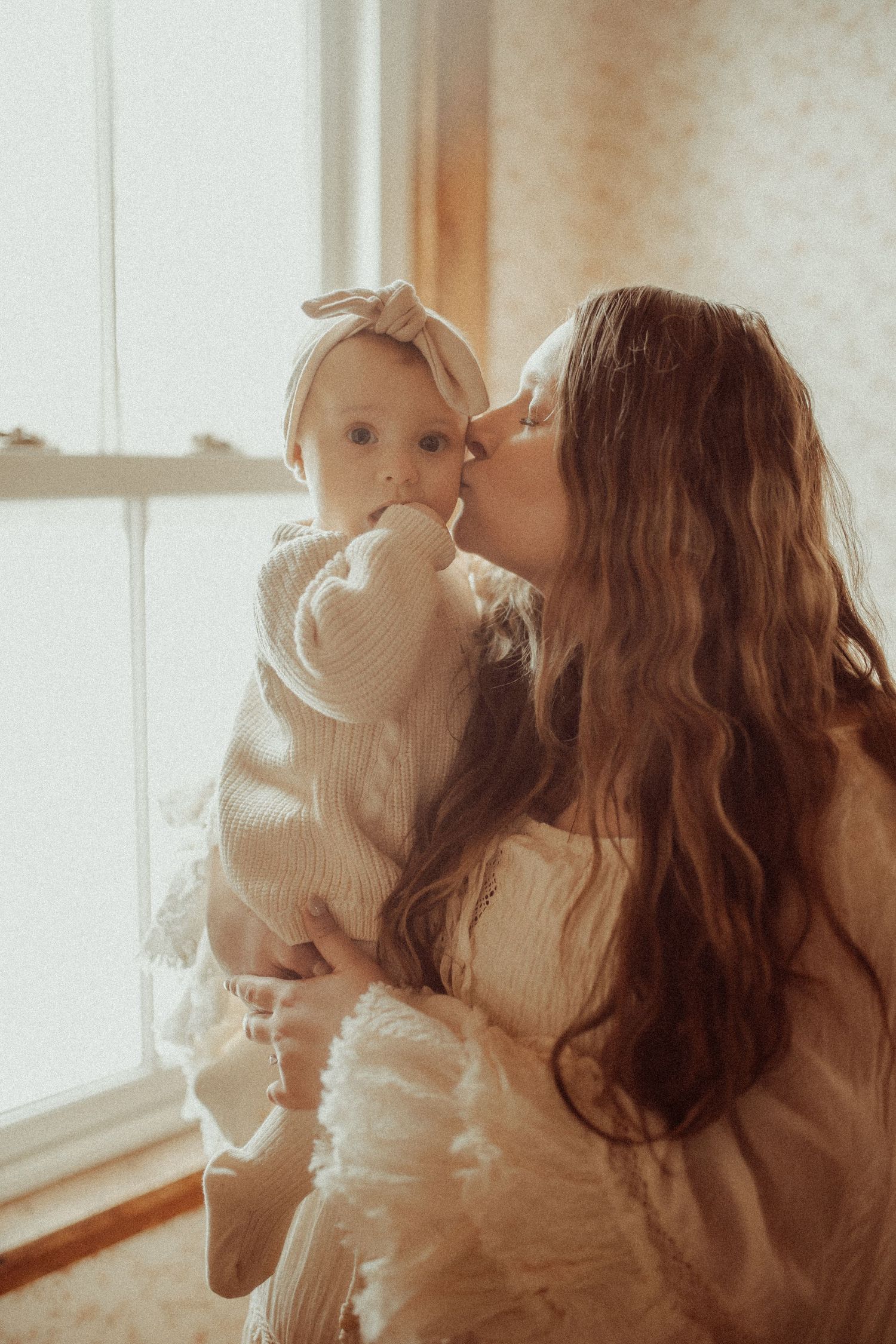Mom nuzzling her baby girls cheek in front of a window with sunlight streaming in for Orono, ON family photographer.