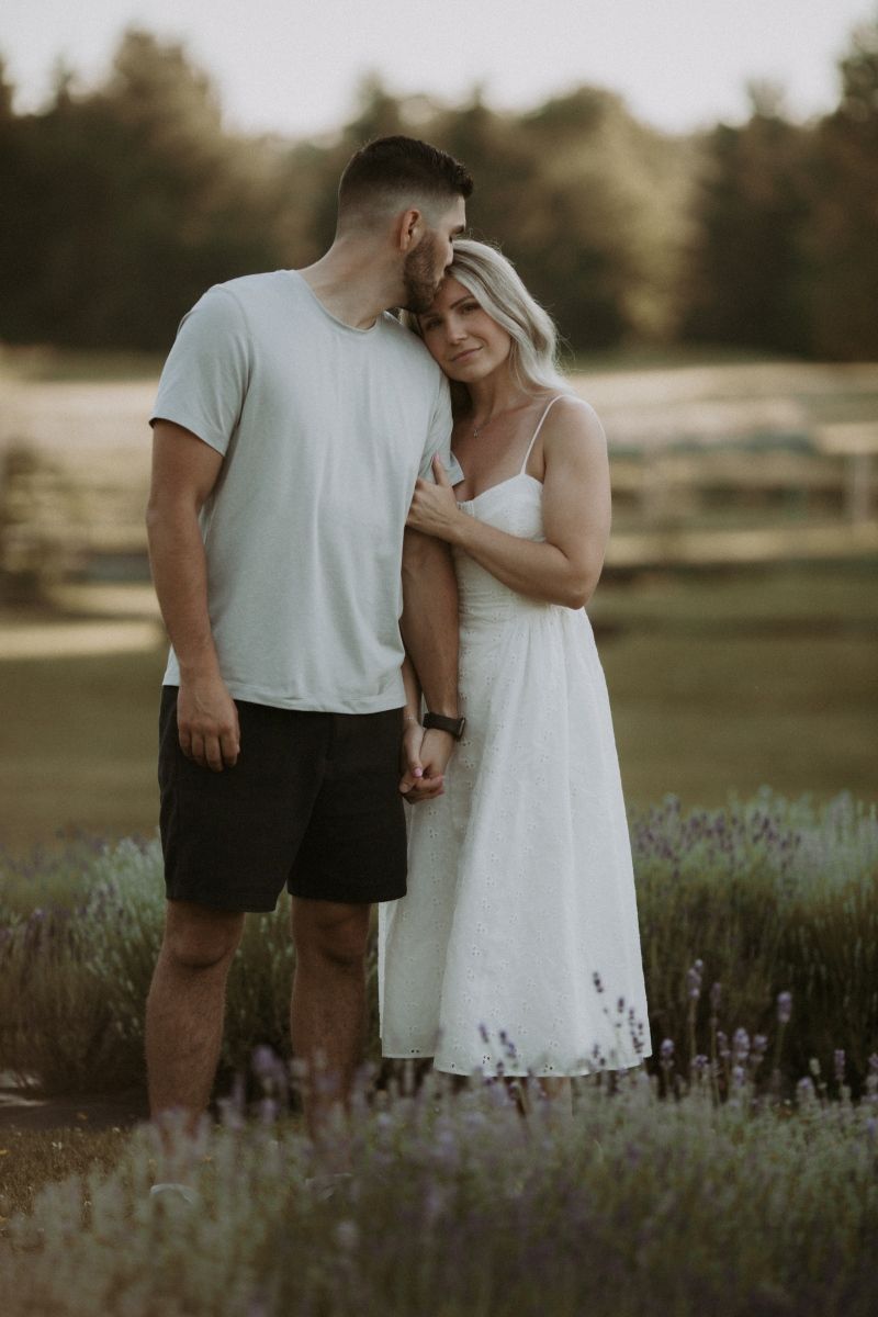 Engaged couple standing close together in a lavender field, sharing a romantic moment by artistic family photographer Bowmanville, ON