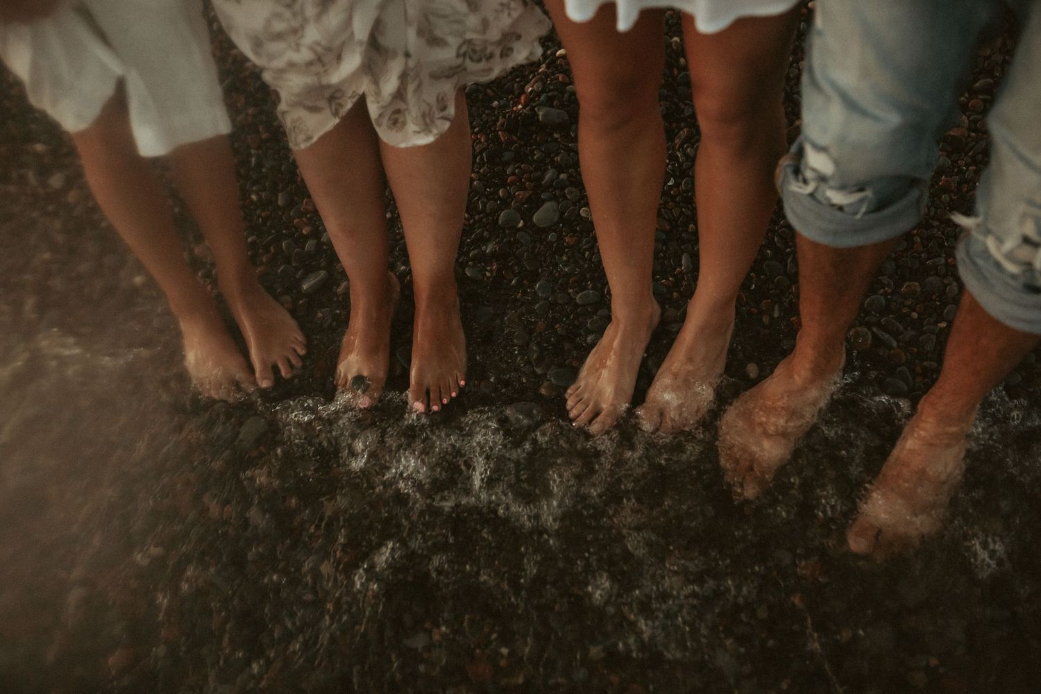 A group of people's feet standing together in a circle in the waves taken by a Bowmanville, ON family photographer.