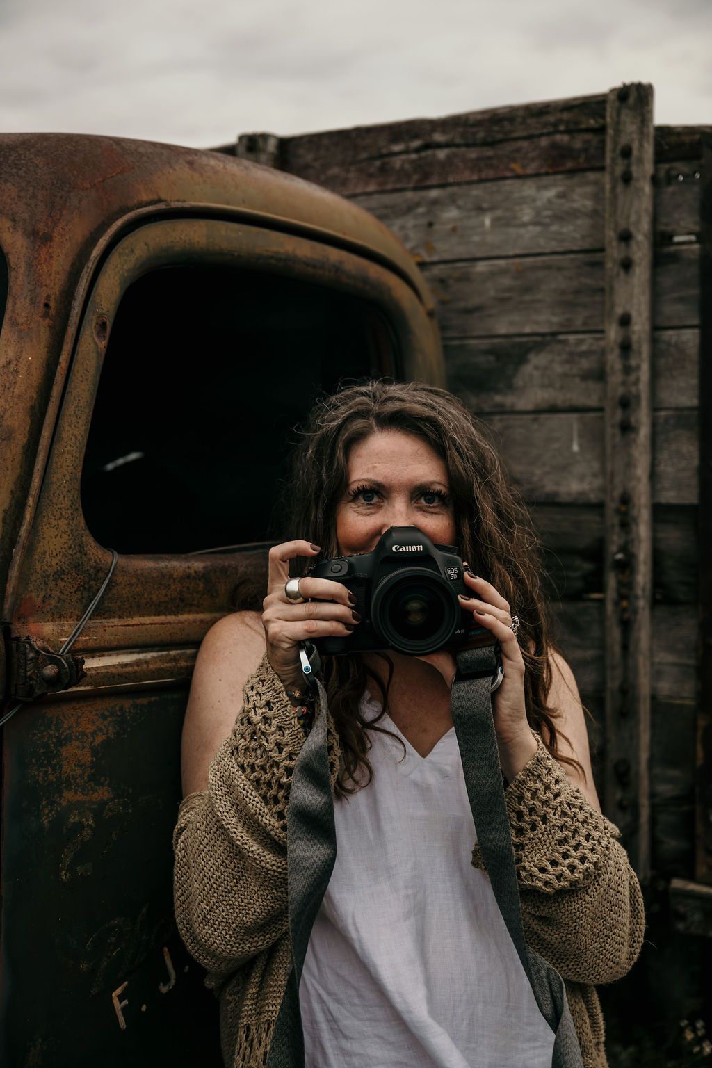 Your Bowmanville, ON family photographer with  camera posed beside rustic wooden barn and antique truck.