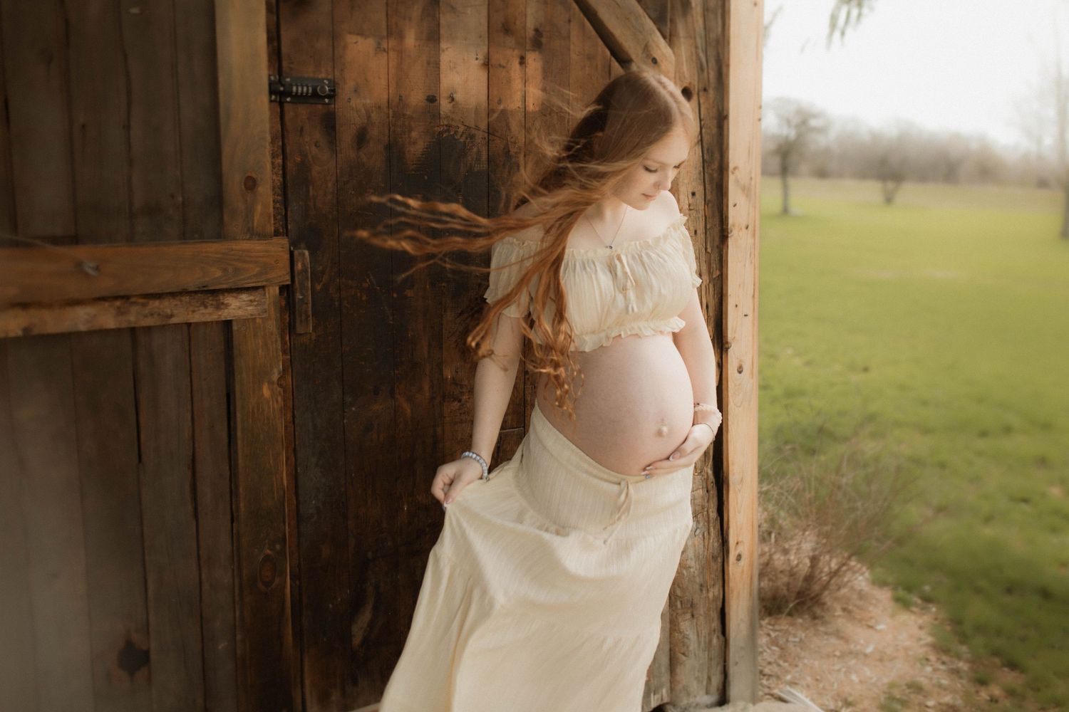 Bowmanville Photography maternity session with a mom holding her baby bump standing against a  barn.