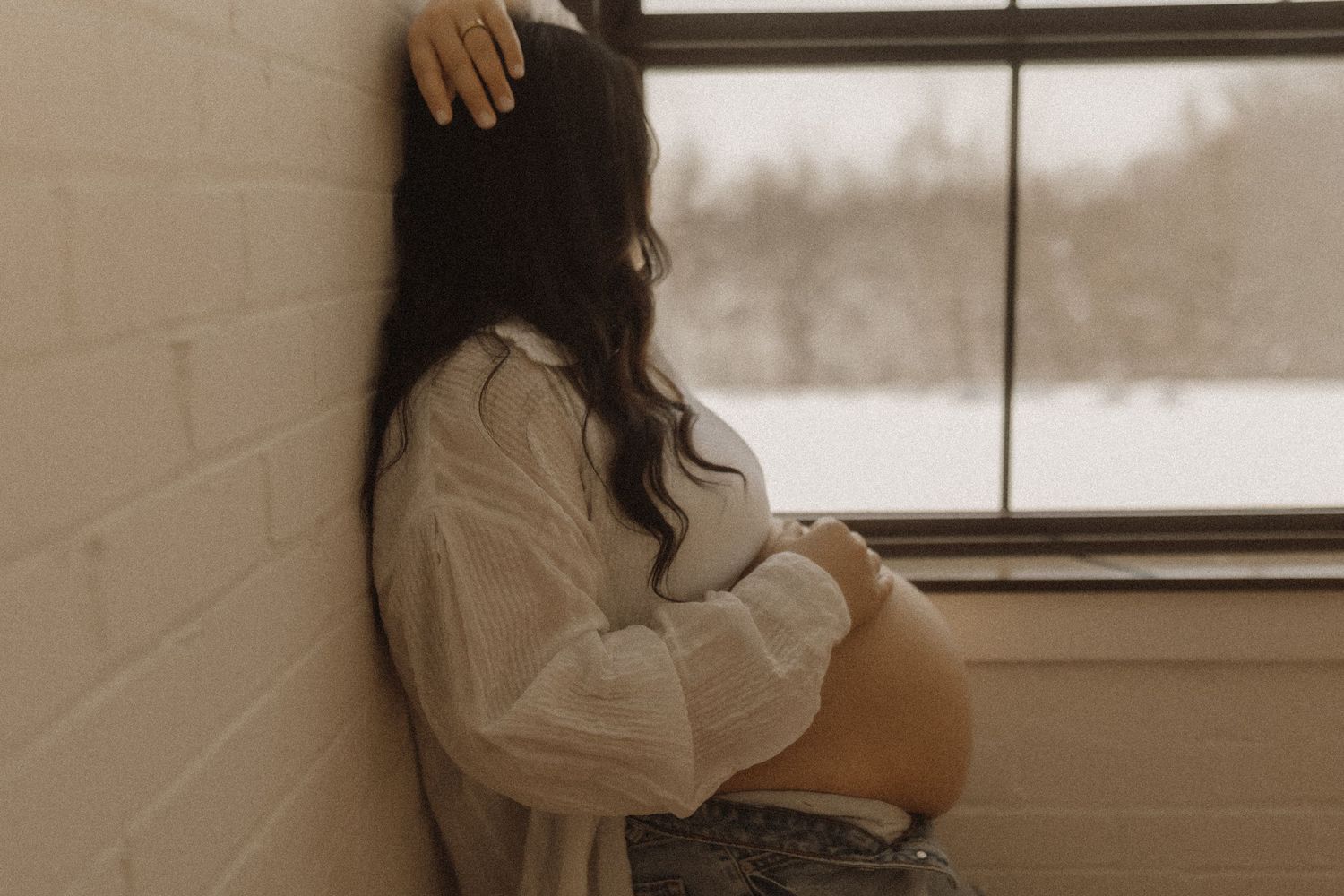 Maternity session in a studio with a mama gently holding her baby bump in front of a window by Bowmanville, ON family photographer.