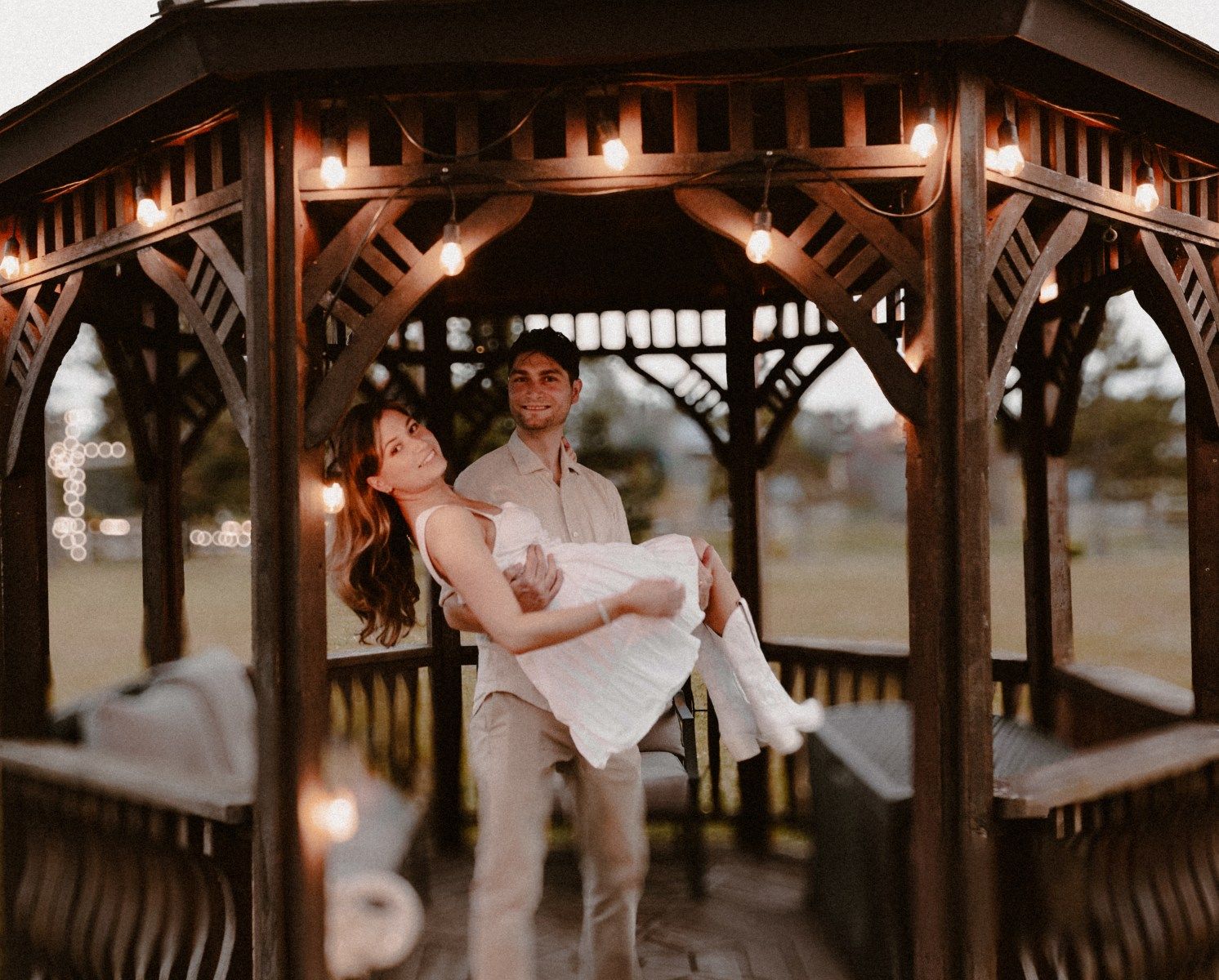 Couple in a gazebo adorned with twinkle lights, sharing an intimate moment, by artistic family photographer Bowmanville, ON.