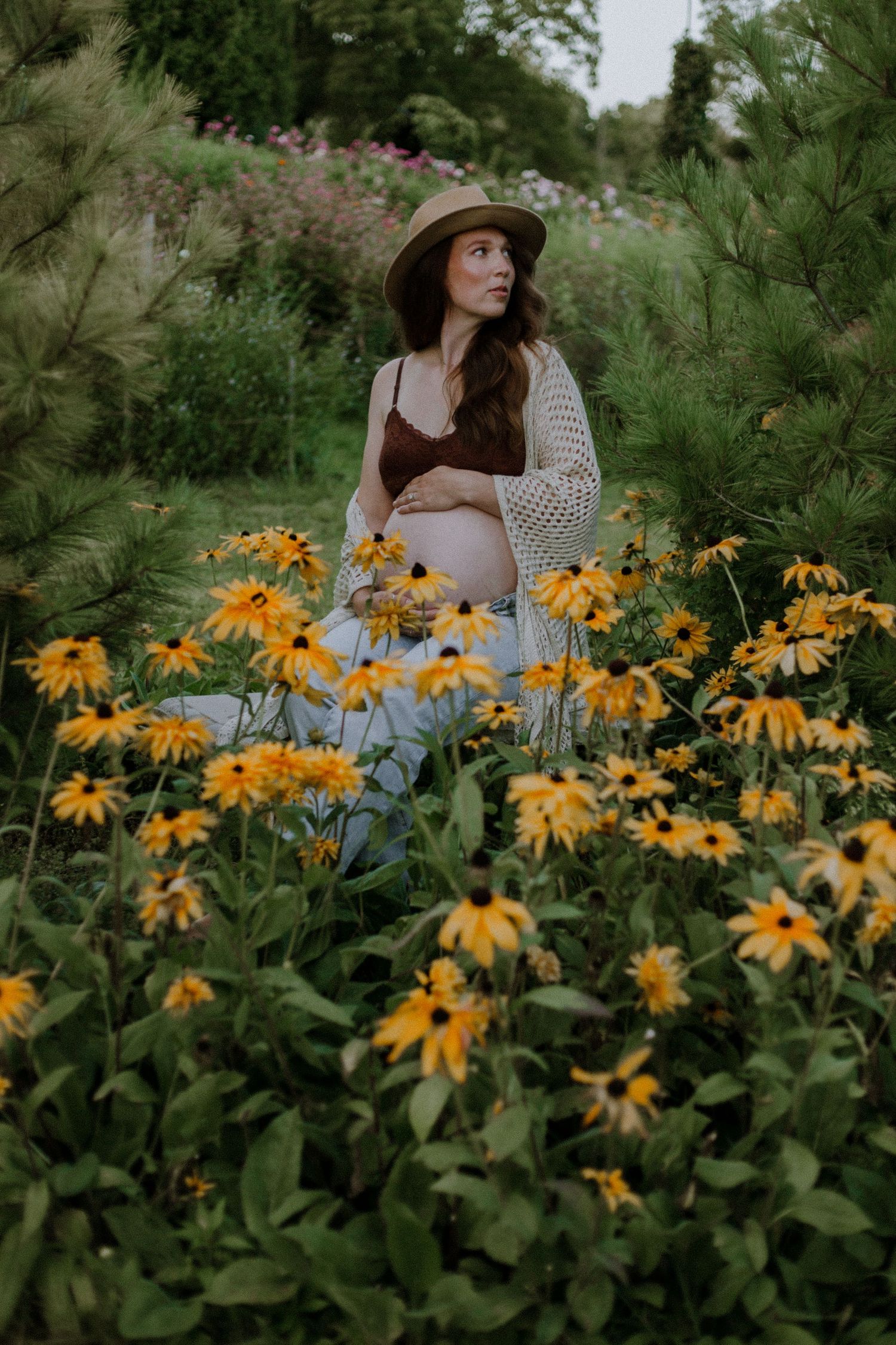 Pregnant woman holding her baby bump in a field of yellow flowers taken by Bowmanville Family Photographer