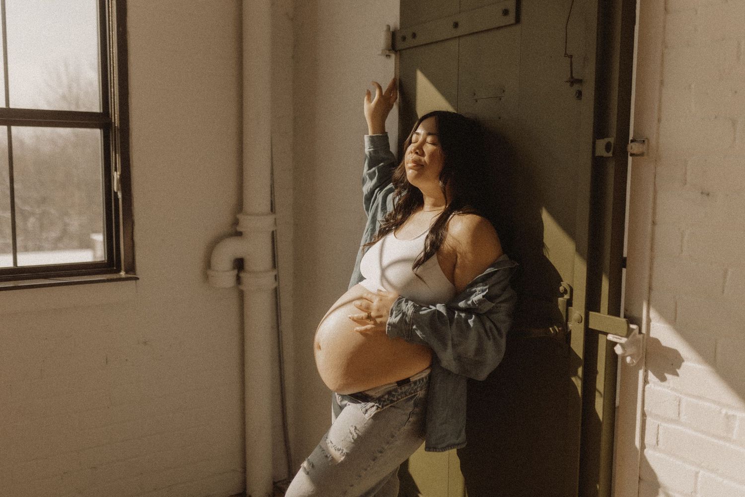 Maternity session in harsh light of a pregnant mom leaning against an industrial factory door by Bowmanville, ON. Family photographer