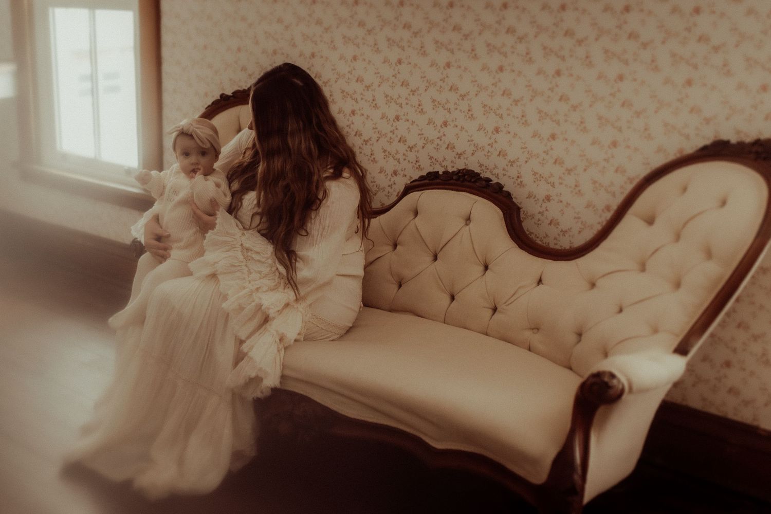 Mom and baby cuddling on an old-fashioned couch in a wallpapered room.  Orono, ON family photographer captured these tender moments
