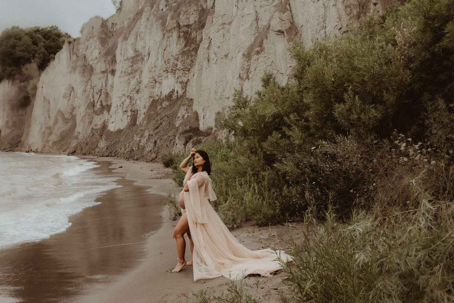 Beautiful mom to be cradling her baby bump on the shore by Durham Region maternity photographer