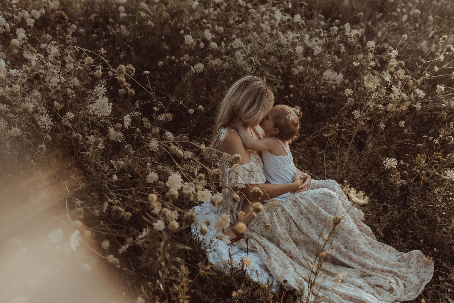 An image of a mother holding her daughter on her lap with their faces close together in a field by a Durham Region maternity photographer