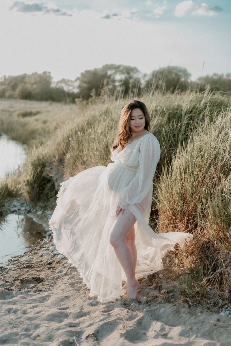 Pregnant woman in a flowy dress standing in the sunshine, taken by Bowmanville, ON family photographer