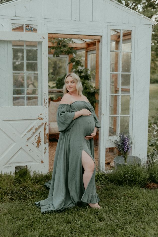 Glowing mama gently holding her baby bump outside a rustic shed in an intimate maternity session.