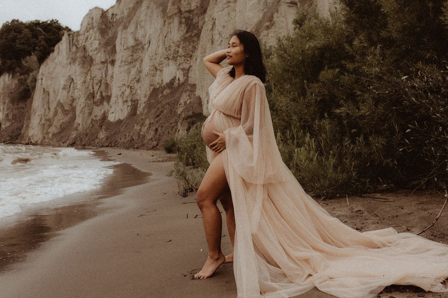 Expectant mom holding a pose on the beach in front of the cliffs by Durham Region maternity photographer