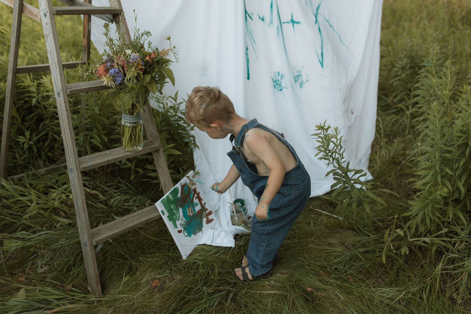 A young boy intently paints a picture on a canvas as he stands in front of a white sheet by Courtice family photographer