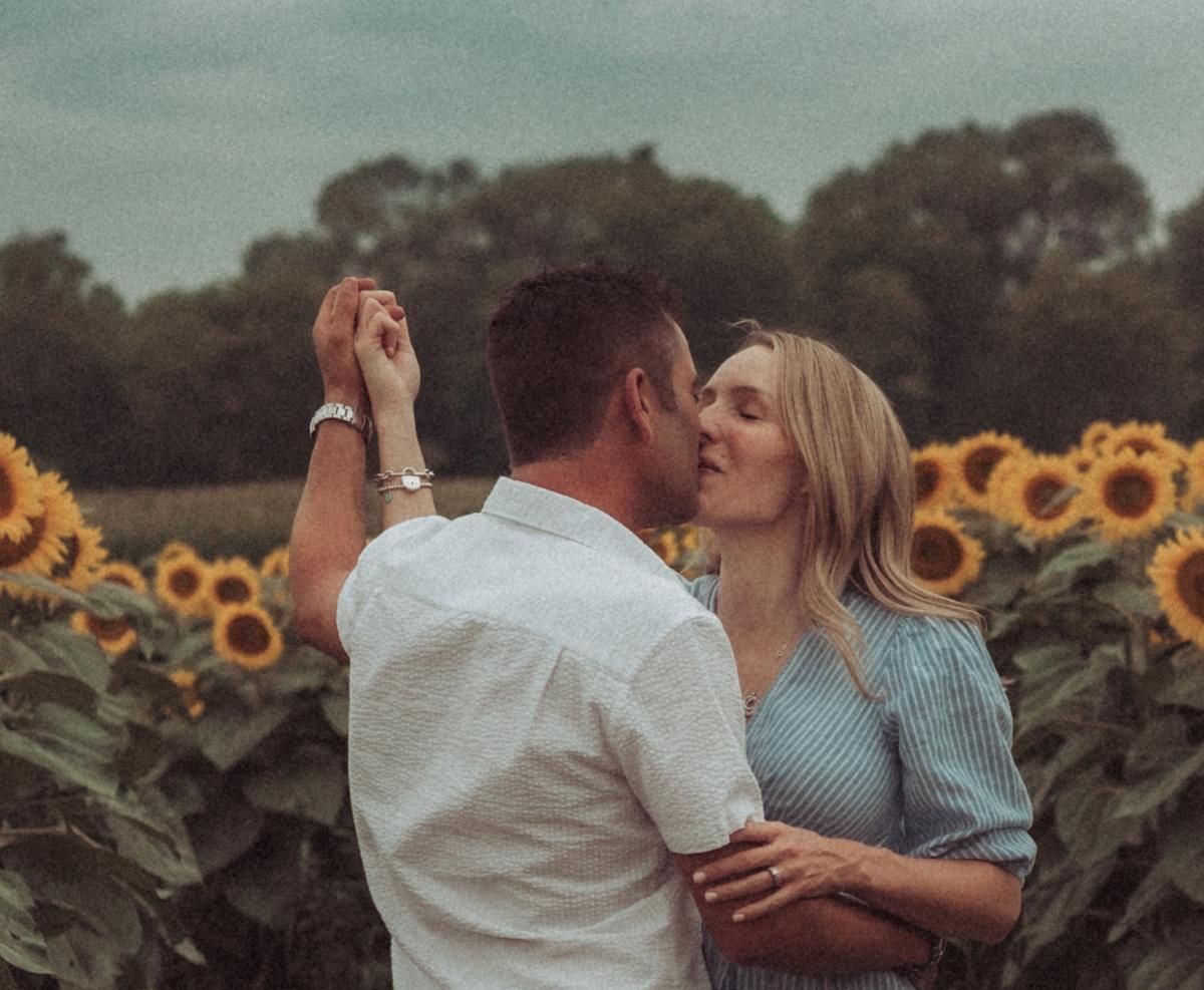 Couple dancing together in a sunflower field, surrounded by tall blooms and golden sunlight, sharing a joyful and romantic moment.