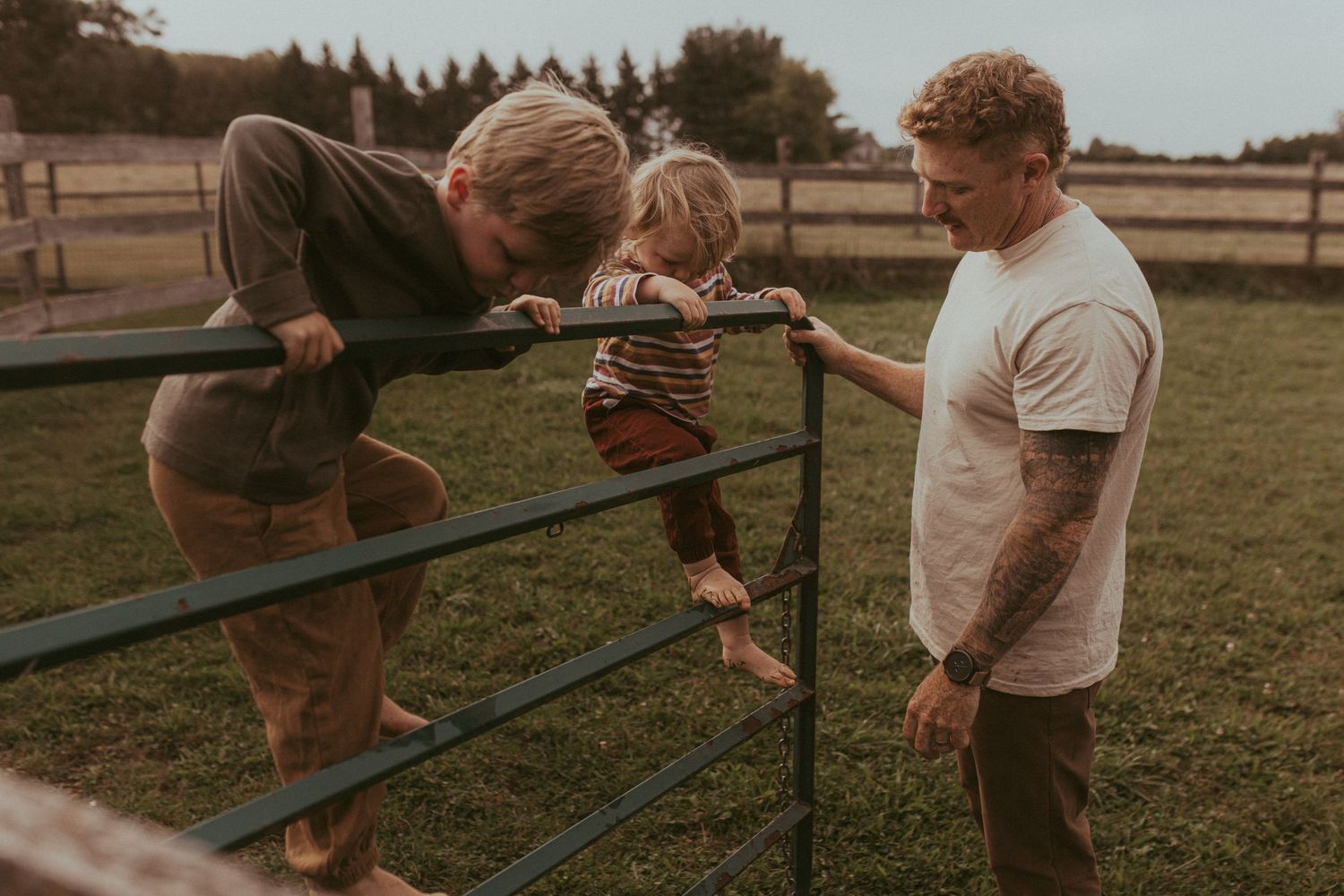 A wide-shot of two boys climbing the gate as their dad gives them a hand by Durham Region family lifestyle photographer.