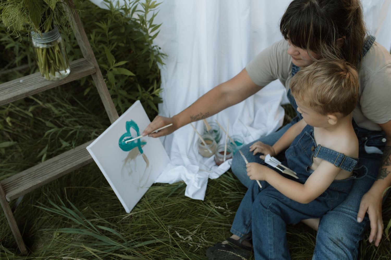 A mom paints a heart on a canvas while her son watches beside her during a painting photo session by Courtice family photographer