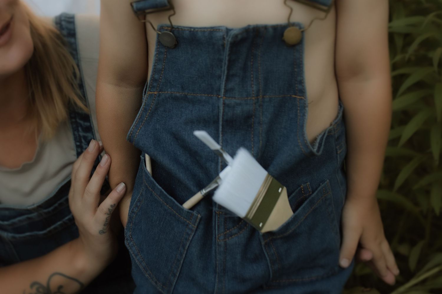 A cropped-in image of a boy holding paint brushes in his overall pockets before he begins painting by Courtice family photographer