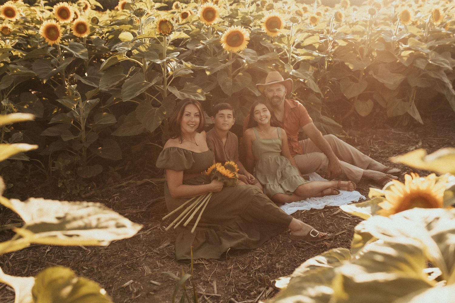 A photo of a family sitting on a blanket surrounded by sunflowers by Durham Region family photographer
