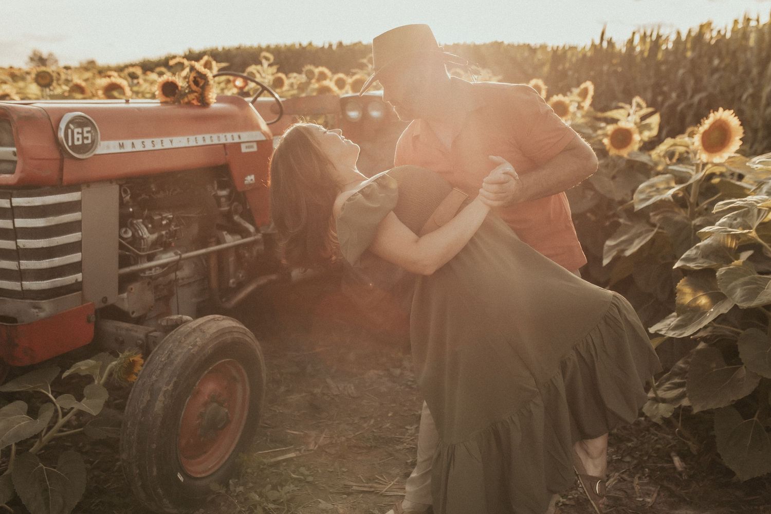 A man dips his wife in the hazy, golden light beside an antique tractor by Durham Region family photographer