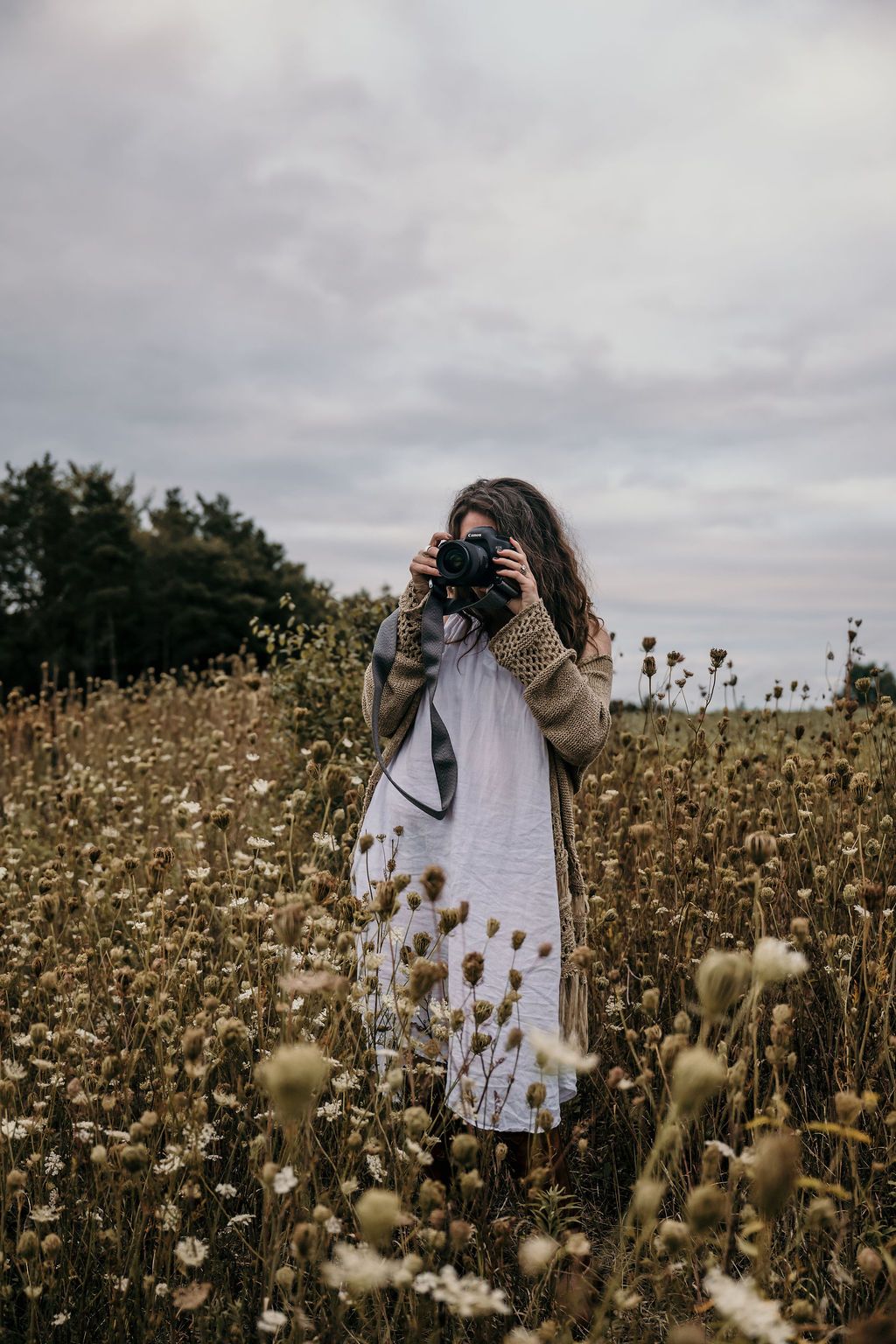 Your Bowmanvile, ON family photographer in a white dress photographing in a field of dried wildflowers under cloudy skies.