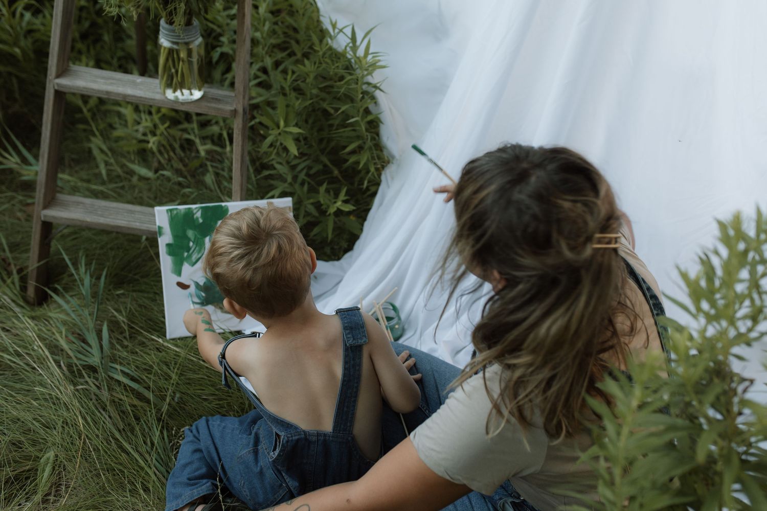 A photo from behind of a mom and son painting together on a canvas by Courtice family photographer