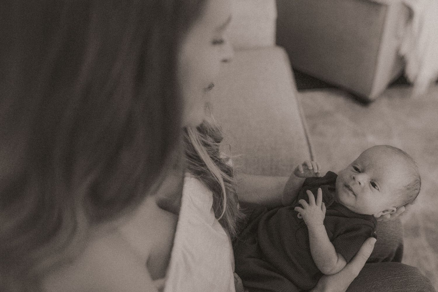 Black and white image of mom gazing at her newborn baby on her lap taken by Bowmanville Family Photographer