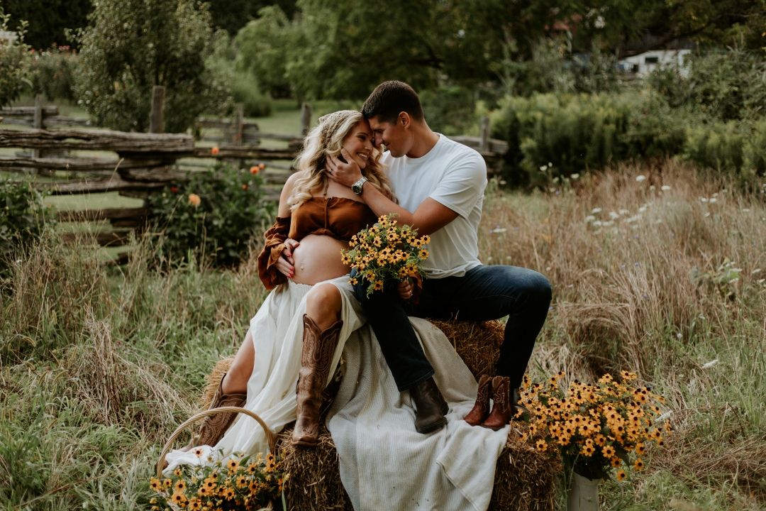 Expecting couple embracing in an emotion-filled outdoor session in a field taken by a Bowmanville, ON family photographer.