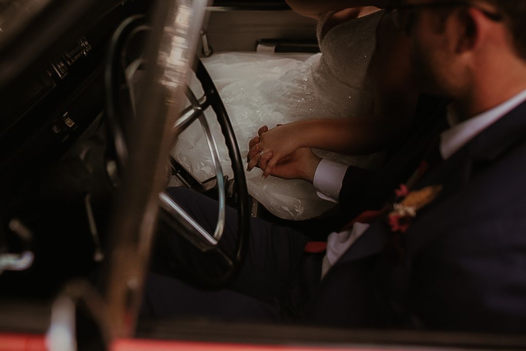Dark and moody shot of a couple holding hands in an old car after their backyard wedding by Cobourg Wedding and Elopement Photographer