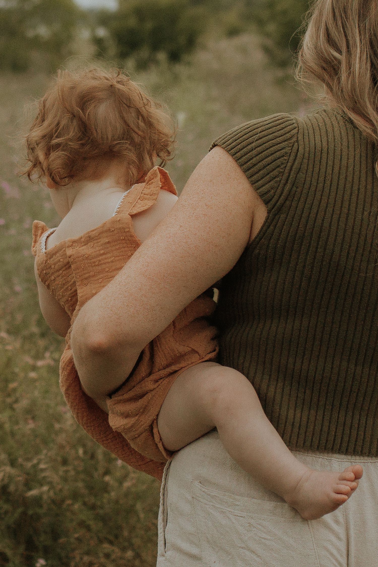 Close-up image of a mom holding her young daughter on her hip as they walk away from the camera by Durham Region maternity photographer