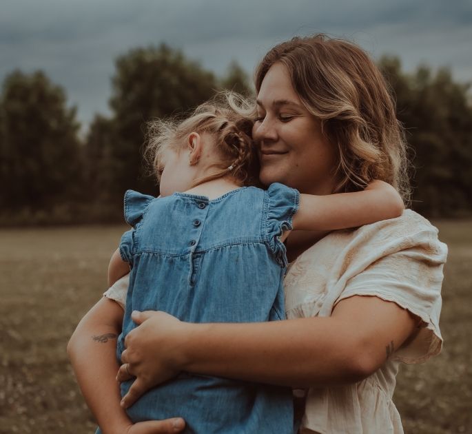 An intimate embrace between a mom and her child captured by your Cobourg, ON family photographer in a field during golden hour
