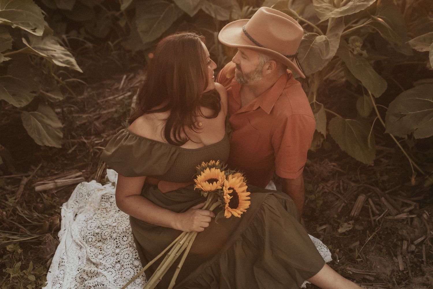 A couple gaze at each other while sitting amongst the sunflowers by Durham Region family photographer